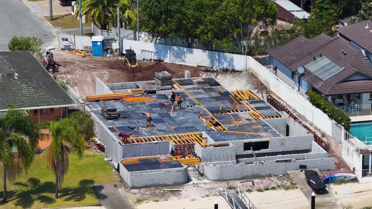 Aerial drone shot of workers preparing timber formwork and concrete slab on sunny suburban construction site
