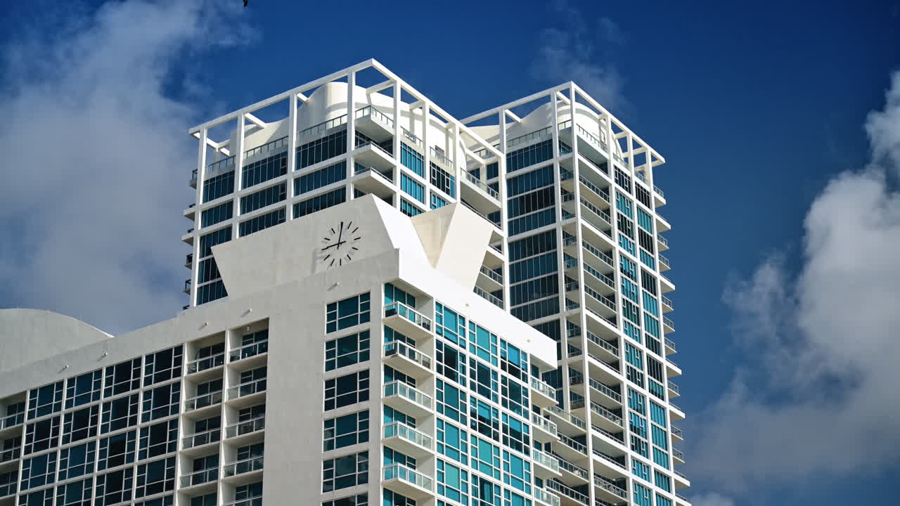 Cima di un moderno grattacielo bianco con orologio a Miami. Vista dal basso dei piani superiori di una torre residenziale bianca con un orologio, contro un cielo blu a Miami Beach.
