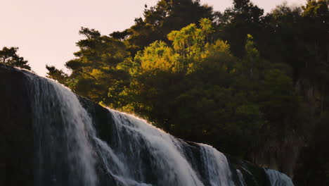 falling waihi waterfall with lighting treetops during sunset in new zealand - slow pan shot