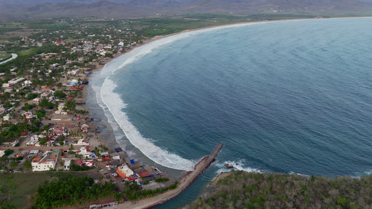 Aerial view of Punta Perula coastline with curved beach, colorful village, and long pier into the ocean