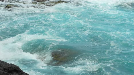 Close-up-of-crystal-clear-waves-flowing-over-rocks-in-a-tropical-ocean