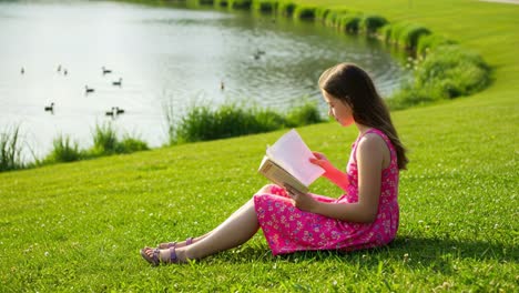 a young girl enjoys reading a book by the serene lakeside, surrounded by lush green grass and swimming ducks, embracing the joy of solitude in nature's beauty