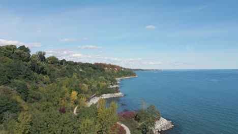 a drone shot of a forest against a lake on a clear sunny day, bluffers park and beach in ontario canada