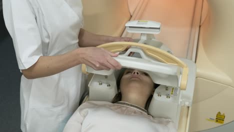 doctor radiologist prepares female patient for brain mri scanning, puts modern equipment, coil on the patient's head.