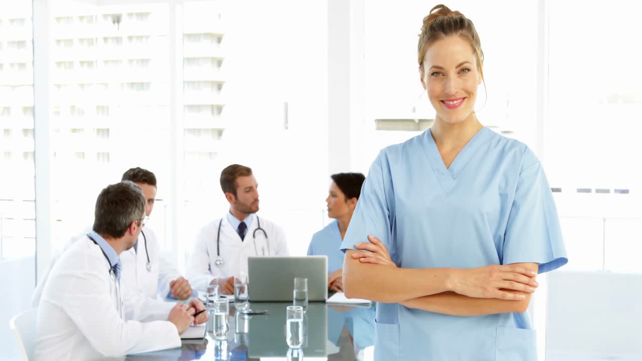 enfermera sonriendo a la cámara mientras el personal está trabajando detrás de ella