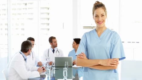 Nurse-smiling-at-camera-while-staff-are-working-behind-her