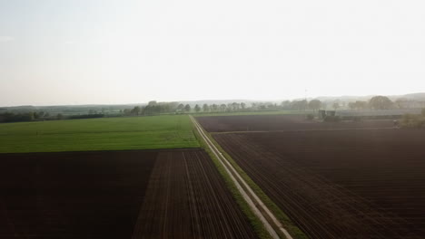 Aerial-view-of-rural-countryside-farmland-being-harvested-and-groomed-for-new-crops-to-grow-during-summer-day