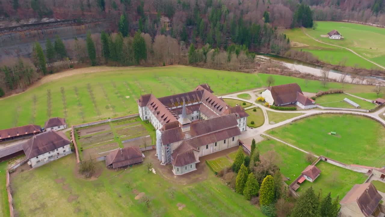 Elokuvamainen lähilennokkilento Abbaye d’Hauteriven yllä lähellä Fribourgia, korostaen yksityiskohtaista luostariarkkitehtuuria ja rauhallista ympäristöä