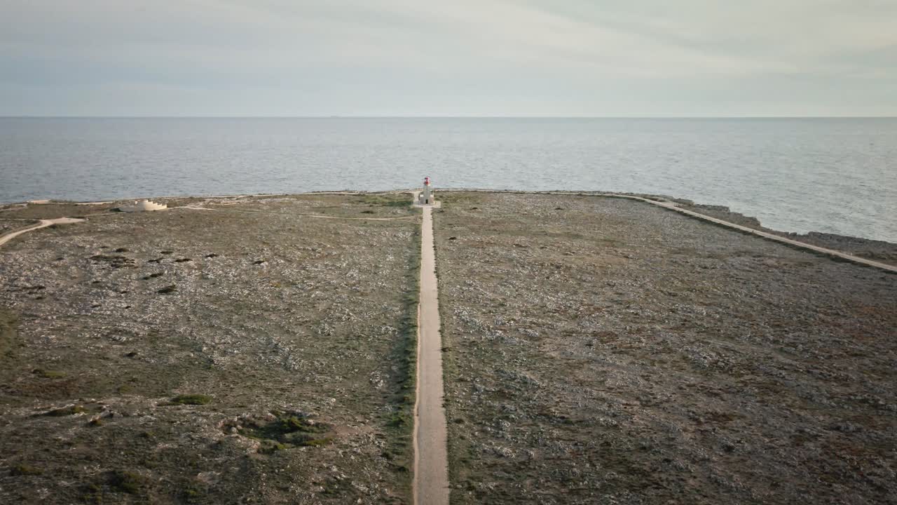 Aerial drone shot gliding forward along a straight path toward a solitary lighthouse, with open cliffs and ocean views in soft daylight