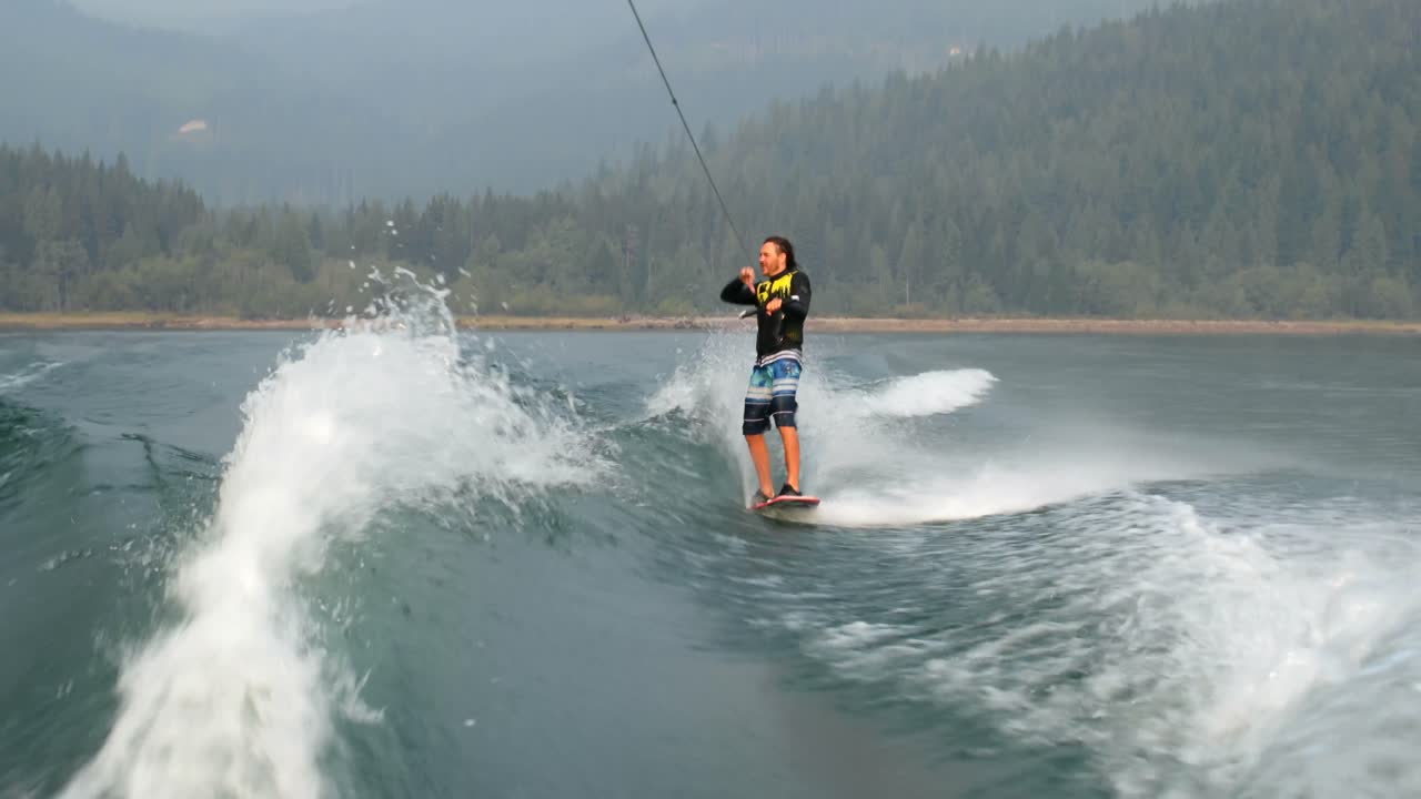 vista frontal de un joven caucásico haciendo trucos en wakeboard en el río de la ciudad 4k