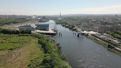 aerial side on pullback of riverside museum and swivelly bridge with glasgow skyline in background, glasgow, scotland, uk