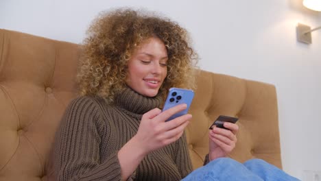 shopping online with credit card and mobile phone. happy white woman making payment in modern smartphone with cheerful smile. customer paying with bank card in shopping app on cellphone
