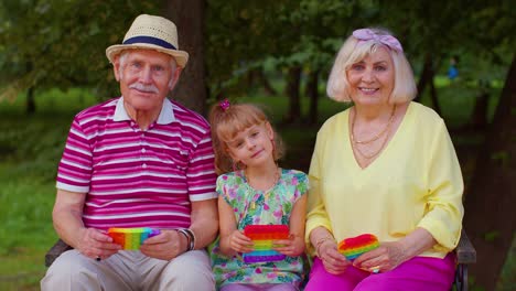 Smiling-senior-grandmother-grandfather-with-granddaughter-playing-squeezing-anti-stress-toy-game