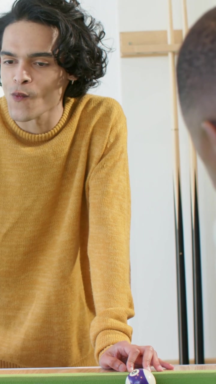Vertical video: Leaning mustard-knit man adjusting, nudging purple ball on felt table rec testing