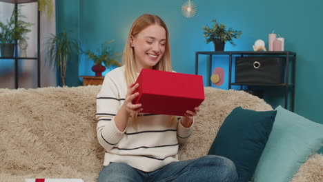 caucasian woman opening birthday surprise gift on sofa smiling excited indoors happy joyful reaction