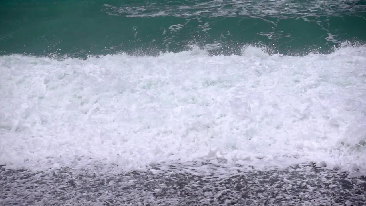 Storm waves powerfully crash against a pebble beach in slow motion capturing the raw force of nature