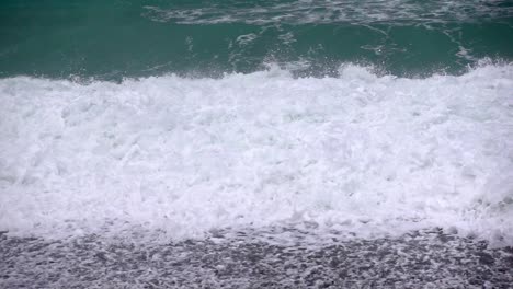 Storm waves powerfully crash against a pebble beach in slow motion capturing the raw force of nature