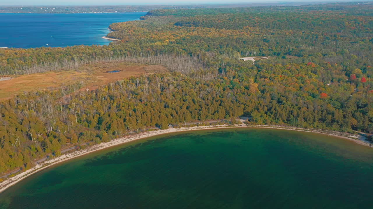The shoreline of Door County, Wisconsin, curves around a calm green bay bordered by dense autumn forest, where warm fall colors meet the blue expanse of Lake Michigan