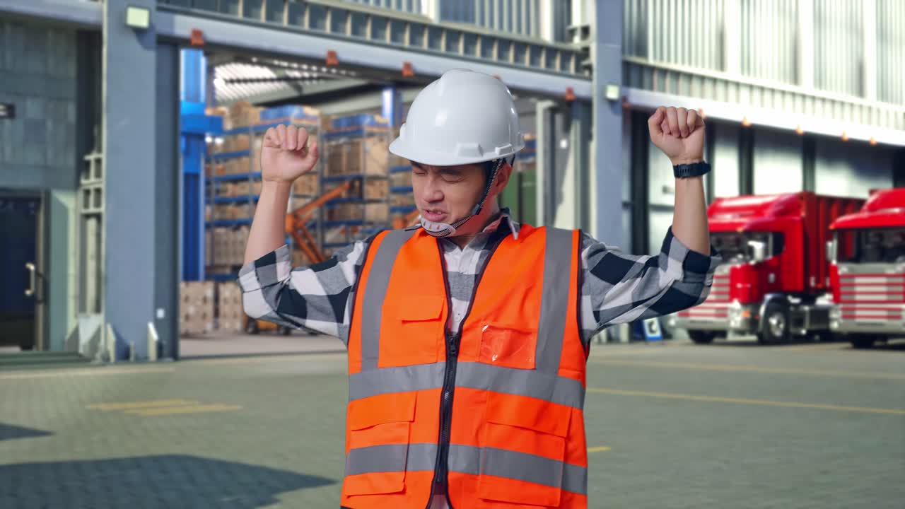 Asian Male Engineer With Safety Helmet Screaming Goal And Dancing Celebrating , Outside of Logistics Distributions Warehouse