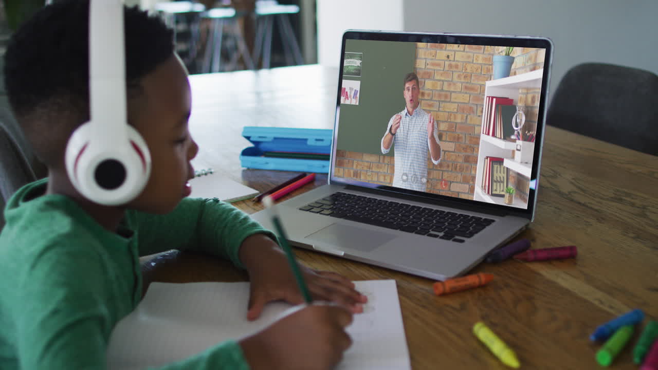 African american boy doing homework while having a video call with male teacher on laptop at home