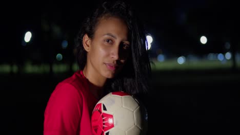 un fútbol es sostenido por una chica joven en un bikini a medida que cae la noche