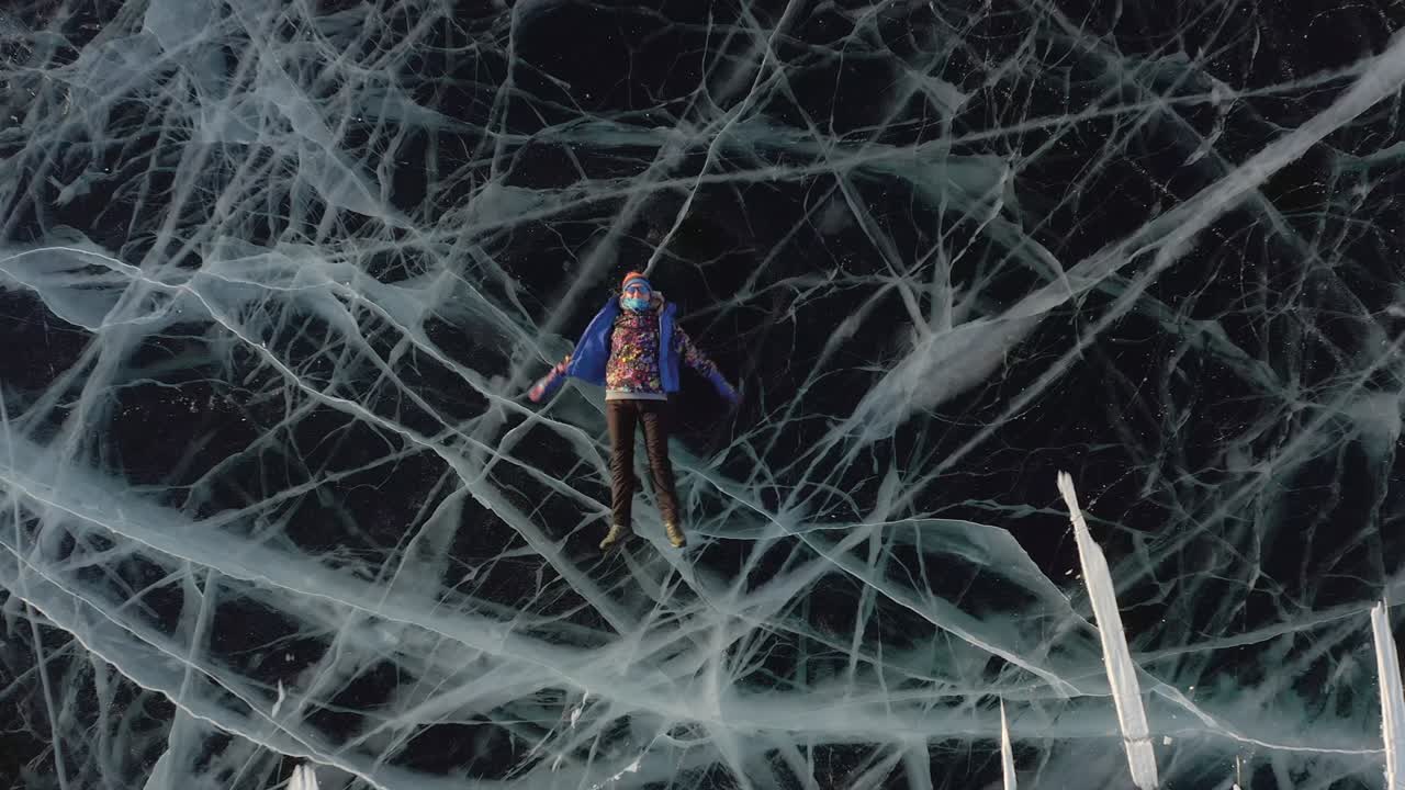 겨울의 한 소녀는 따뜻한 옷을 입고 얼음 위에 누워서 팔과 다리를 으로 흔들며 천사를 묘사합니다.