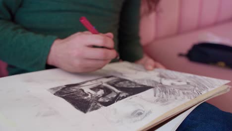 primer plano de la mano del artista hispano borrando la imagen en el bloc de dibujo mientras se sienta en un sofá rosa