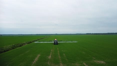 vista aérea del tractor rociando pesticidas y fertilizantes en el campo verde en un día de verano nublado, disparo de drones ascendentes de gran angular avanzando