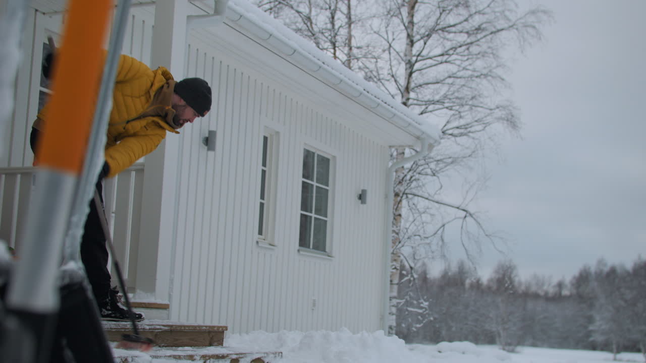 Middle aged man brushing snow from porch on winter day