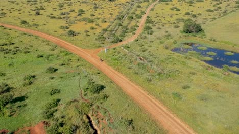 High-pullback-drone-shot-of-mountain-biker-on-a-farm-dirt-road