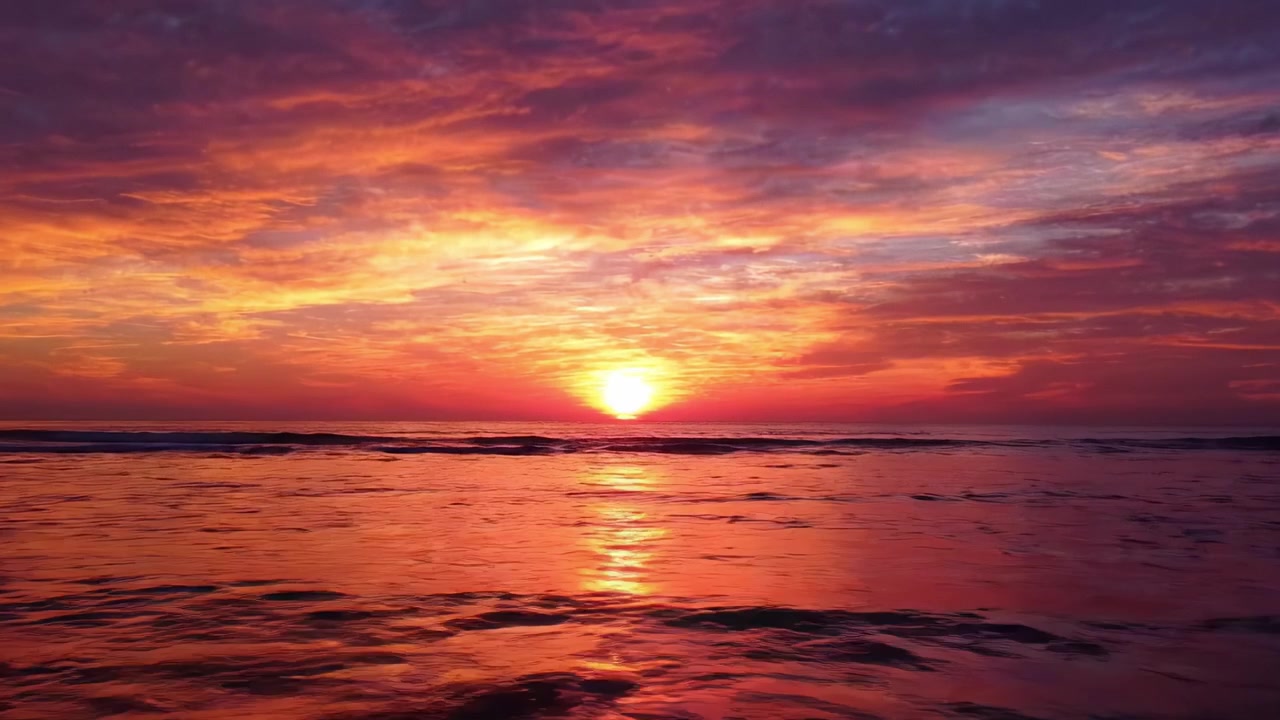 A breathtaking sunset over tranquil waters, capturing the vibrant hues of purple, orange, and pink as the sun dips below the horizon, reflecting on the gentle waves.