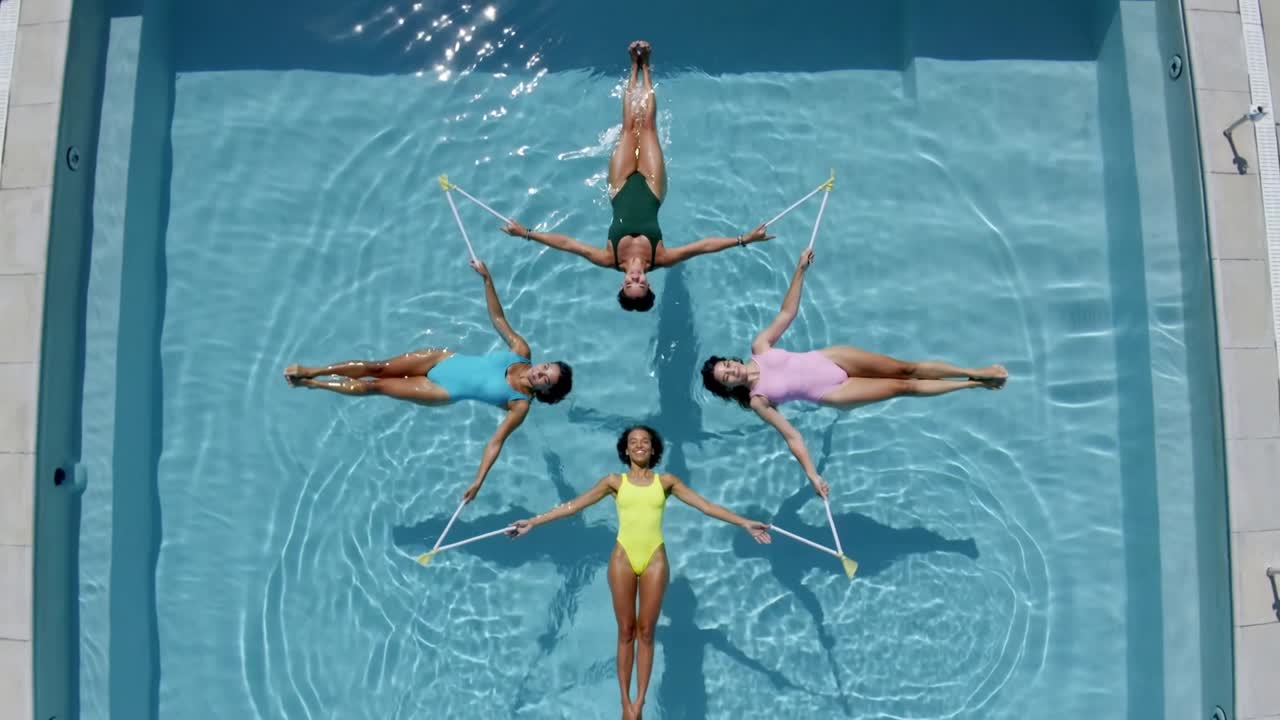 Vídeo vertical: 4 nadadores de maiô flutuando na piscina, segurando molduras, com a câmera recuando para a rotina.