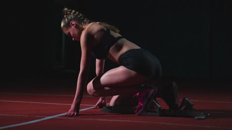 Young-woman-athlete-in-black-shorts-and-a-t-shirt-is-preparing-to-start-in-the-race-for-100-meters-on-the-treadmill-near-the-start-line