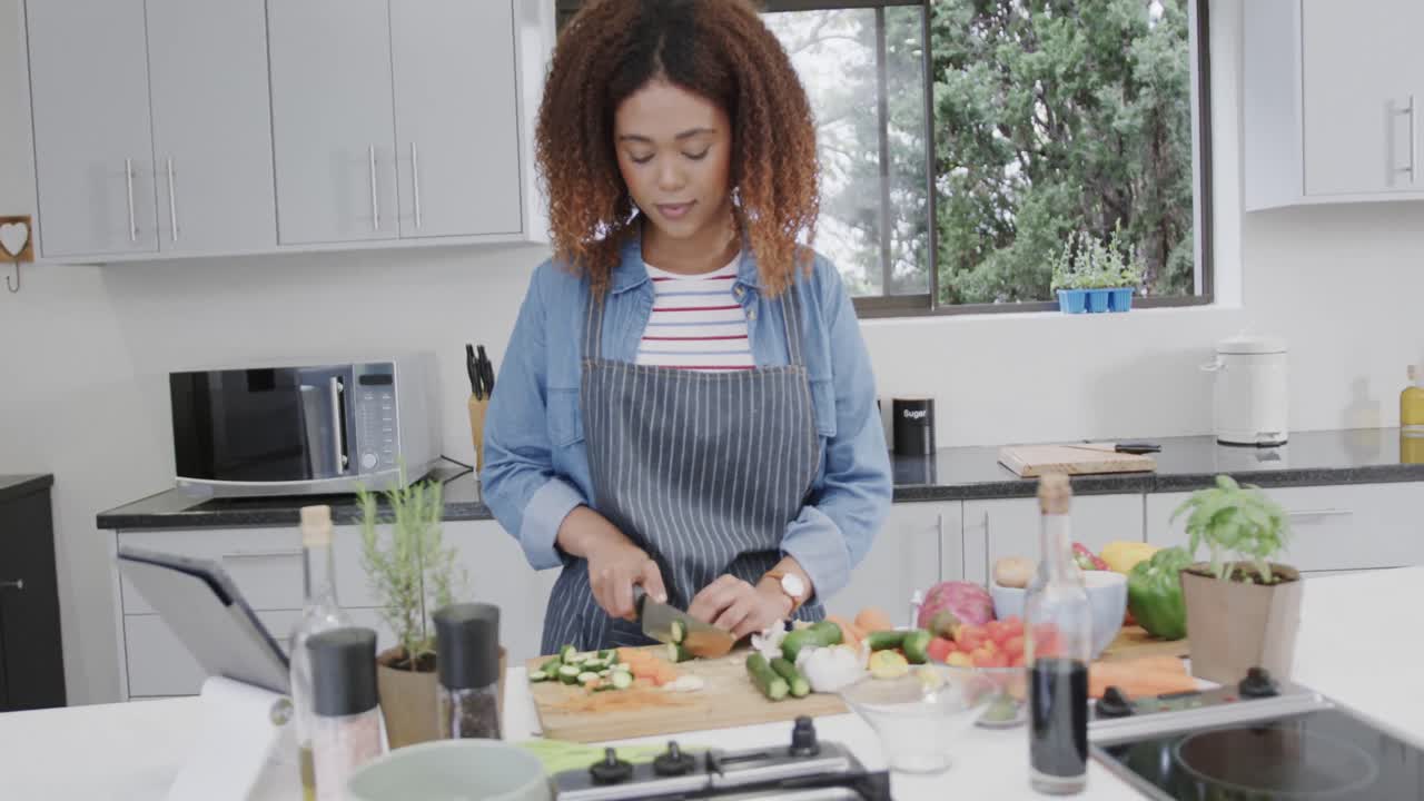 mujer biracial con delantal preparando comida, cortando verduras en la cocina, cámara lenta