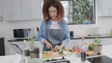 biracial woman wearing apron preparing meal, chopping vegetables in kitchen, slow motion