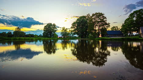 puesta de sol con nubes flotando por sobre un lago con una casa de campo