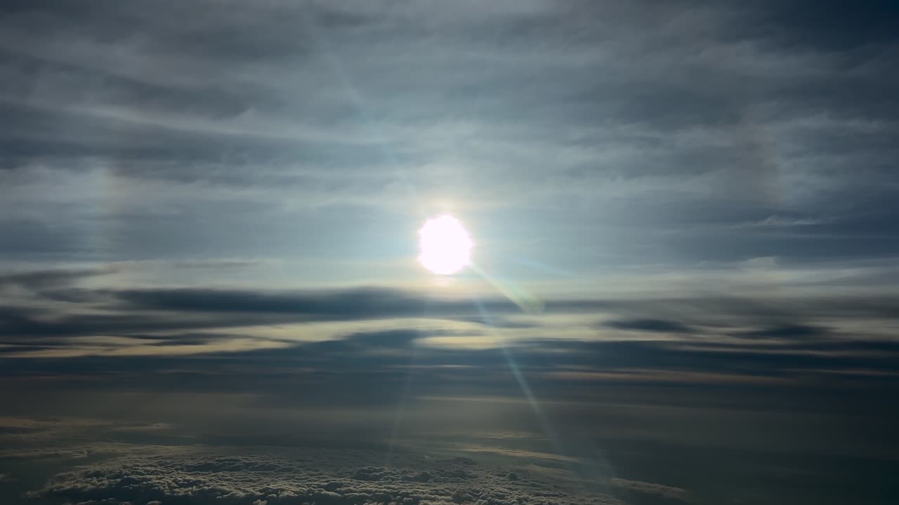 Luftfoto af en glødende sol og dens glorie på en dramatisk himmel, set under flyvning i stratosfæren gennem lag af æteriske skyer.
