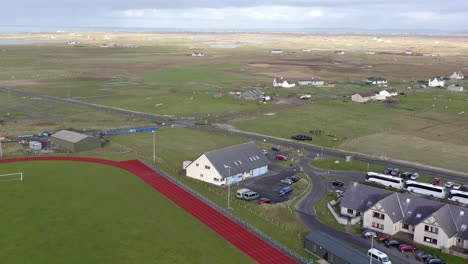 reversing, wide angle drone shot flying above a track and pitch away from the uhi college campus and the dark island hotel on the isle of benbecula