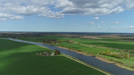 aerial drone video shot of wide green grass field and long river in a village