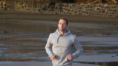 slow motion shot of young caucasian man running on the beach in auckland, new zealand