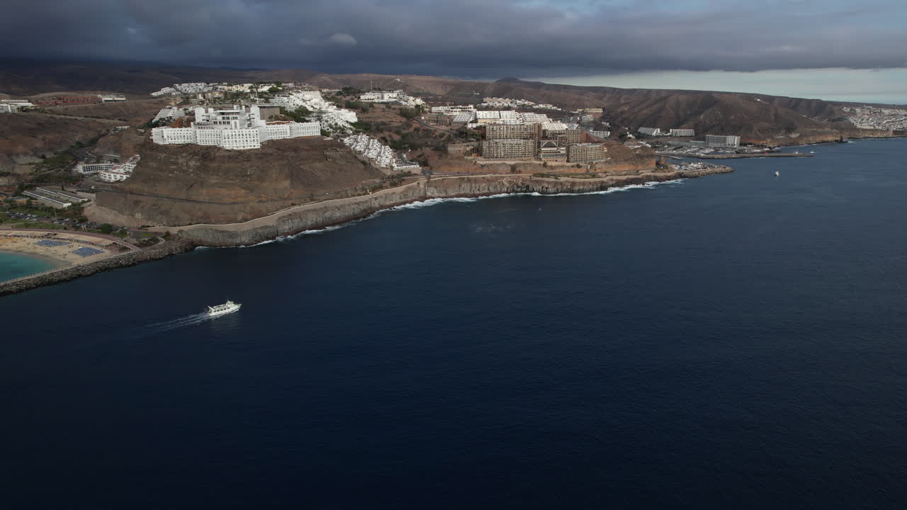 toma aerea siguiendo un barco que navega y al fondo se ve la playa de amadores y los hoteles de la zona