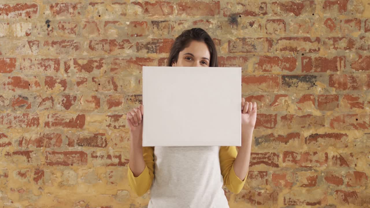 Caucasian woman holding a white rectangle on a brick wall