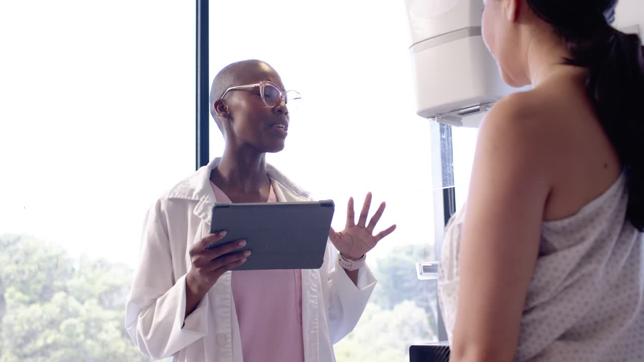 Une clinicienne et une patiente debout dans une salle d'examen, la clinicienne utilisant une tablette pour expliquer le plan de soins.