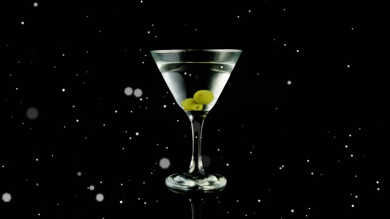 Punti bianchi che fluttuano su olive in un bicchiere da cocktail su sfondo nero.