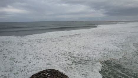 Vista-Aérea-De-Un-Muelle-Rocoso-Con-Playa-De-Arena-Y-Olas-Oceánicas