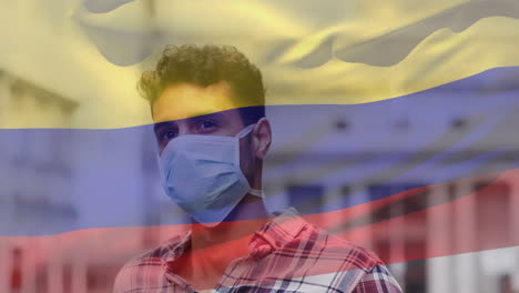 animation of flag of colombia waving over man wearing face mask during covid 19 pandemic