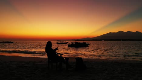 silhouette of girl watching sunset from tranquil exotic beach of famous vacation destination tropical island in indonesia