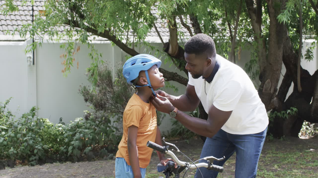 African American father helps son with bike helmet outdoors