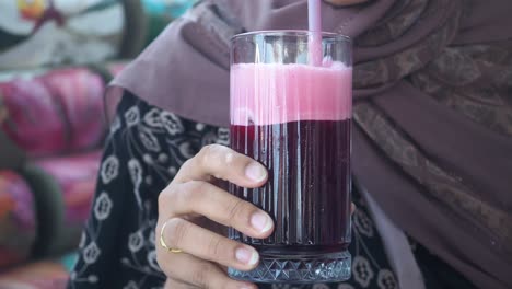 person holding a glass of red juice with pink foam and a straw