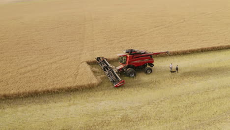 farmers walking away from combine harvester in cut grain field, aerial